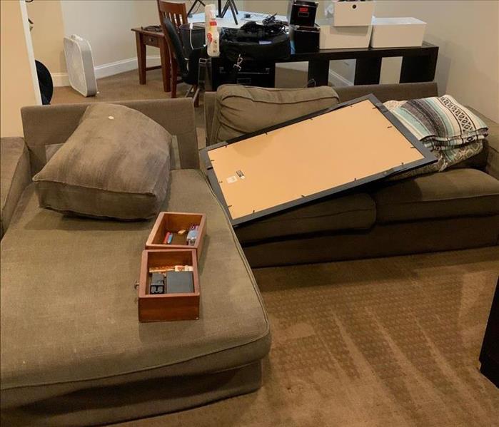 Living area with contents on table and couches. Fans are running near a heavily saturated carpet