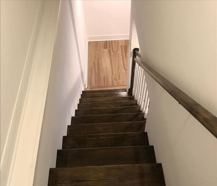 A polished, freshly-repaired stairway with new drywall, steps, and banister near the lower wall. The landing has new wood flo